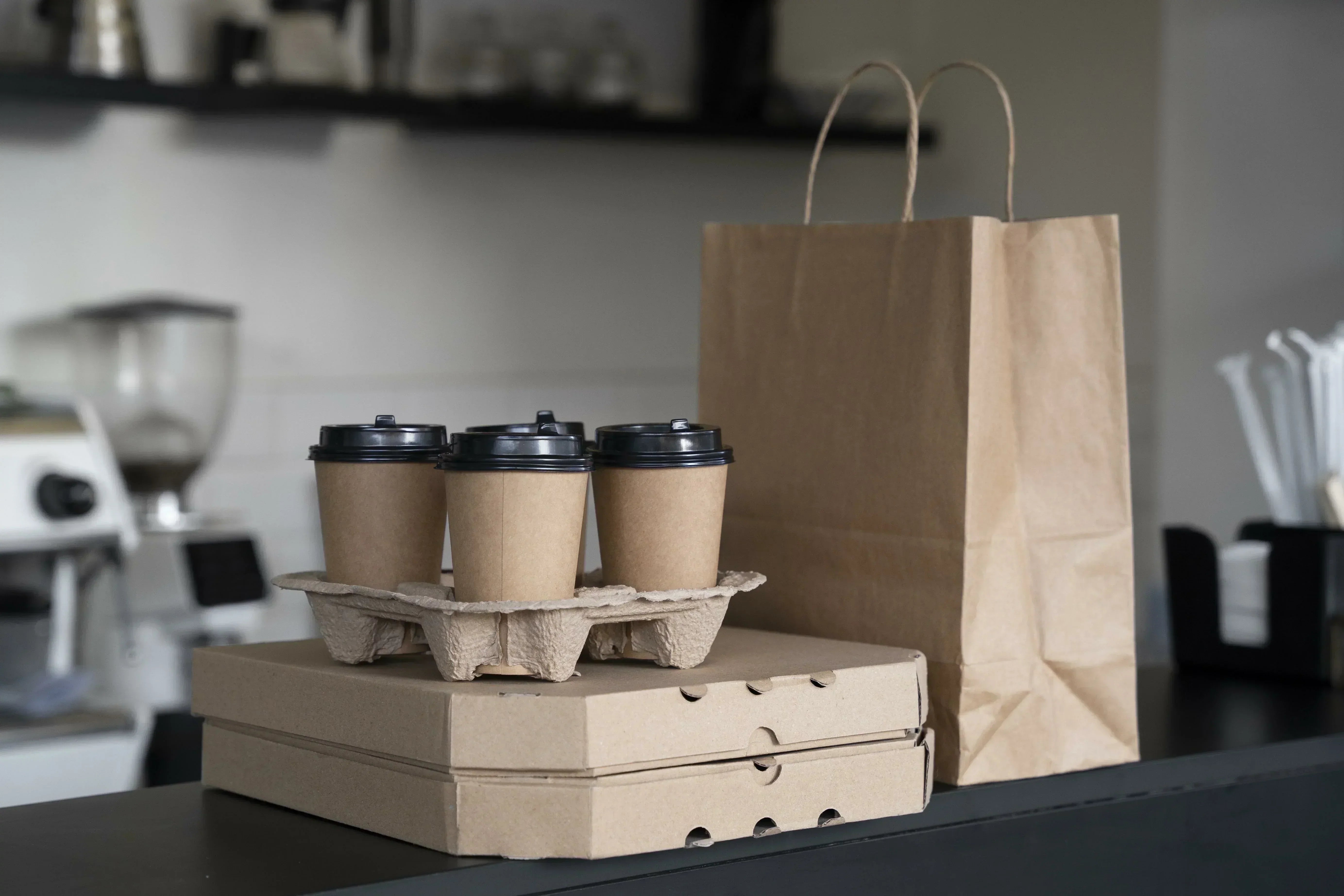 Braune Kaffeebecher, Pizzakartons und eine PapiertĂŒte stehen auf einem Tresen.