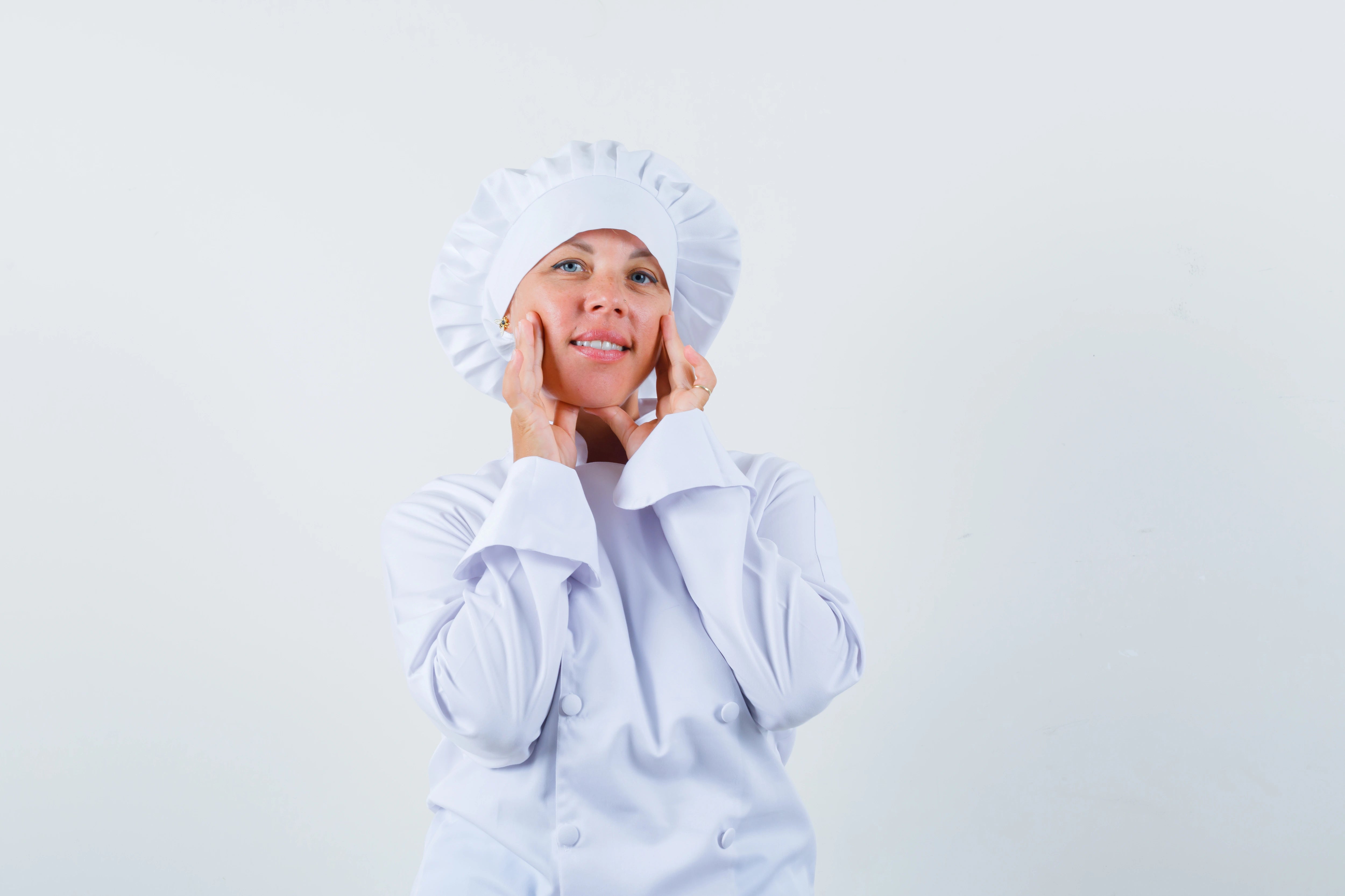 Frau mit Kochmütze vor neutralem Hintergrund.