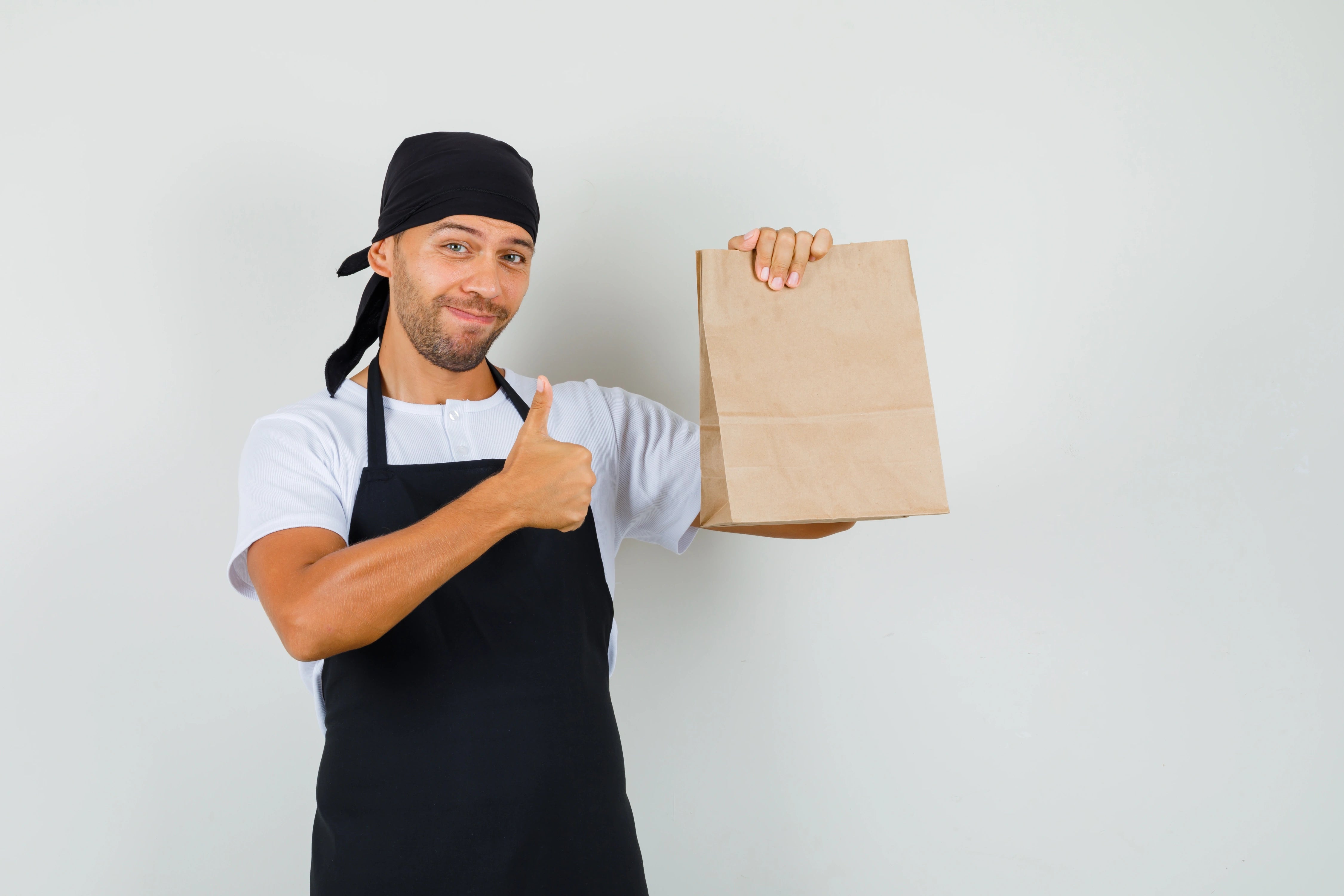 Junger Gastronom, der freundlich eine Papiertragetasche präsentiert.