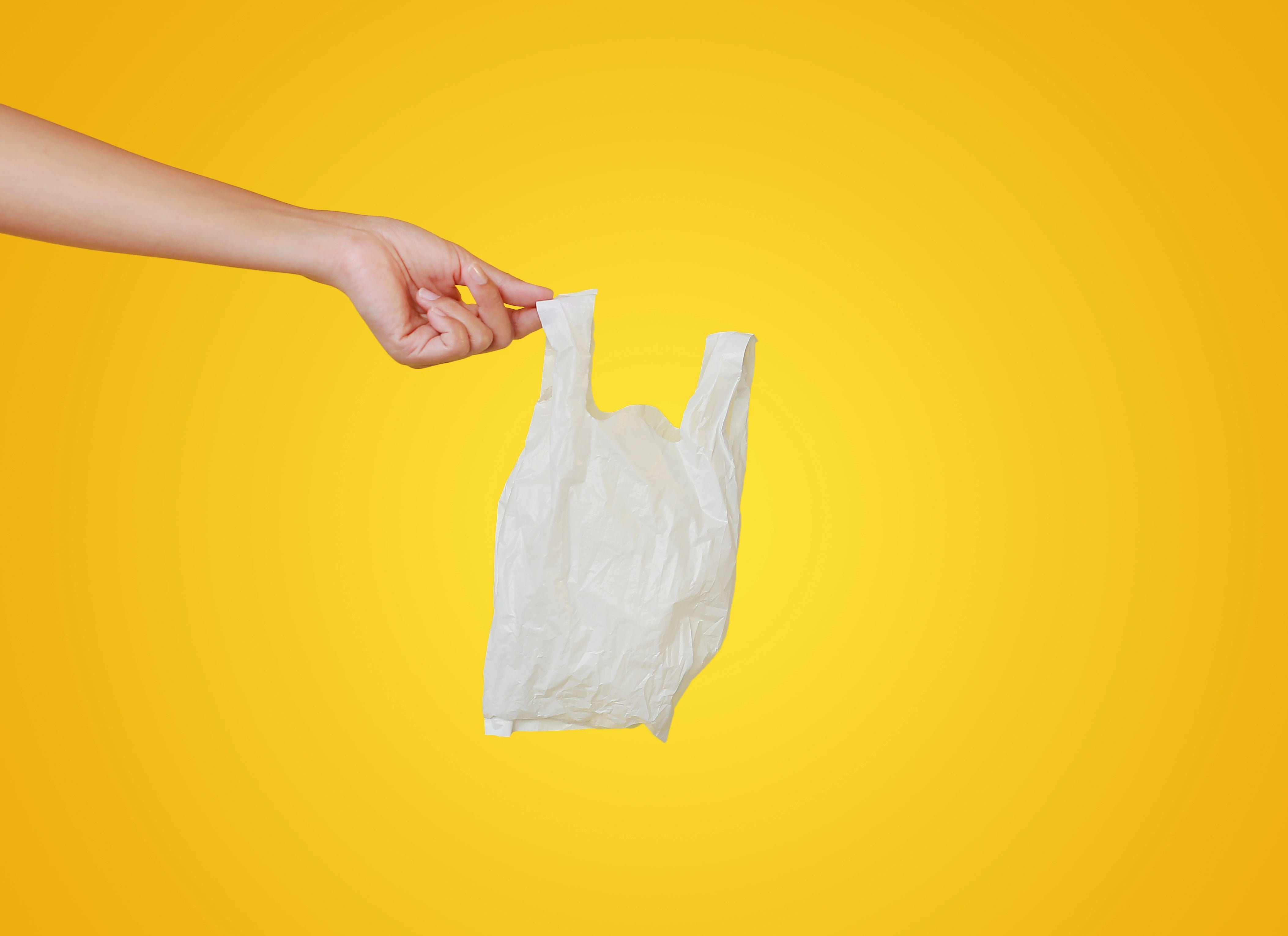 Eine Hand präsentiert einen HDPE Hemdchenbeutel vor gelbem Hintergrund.