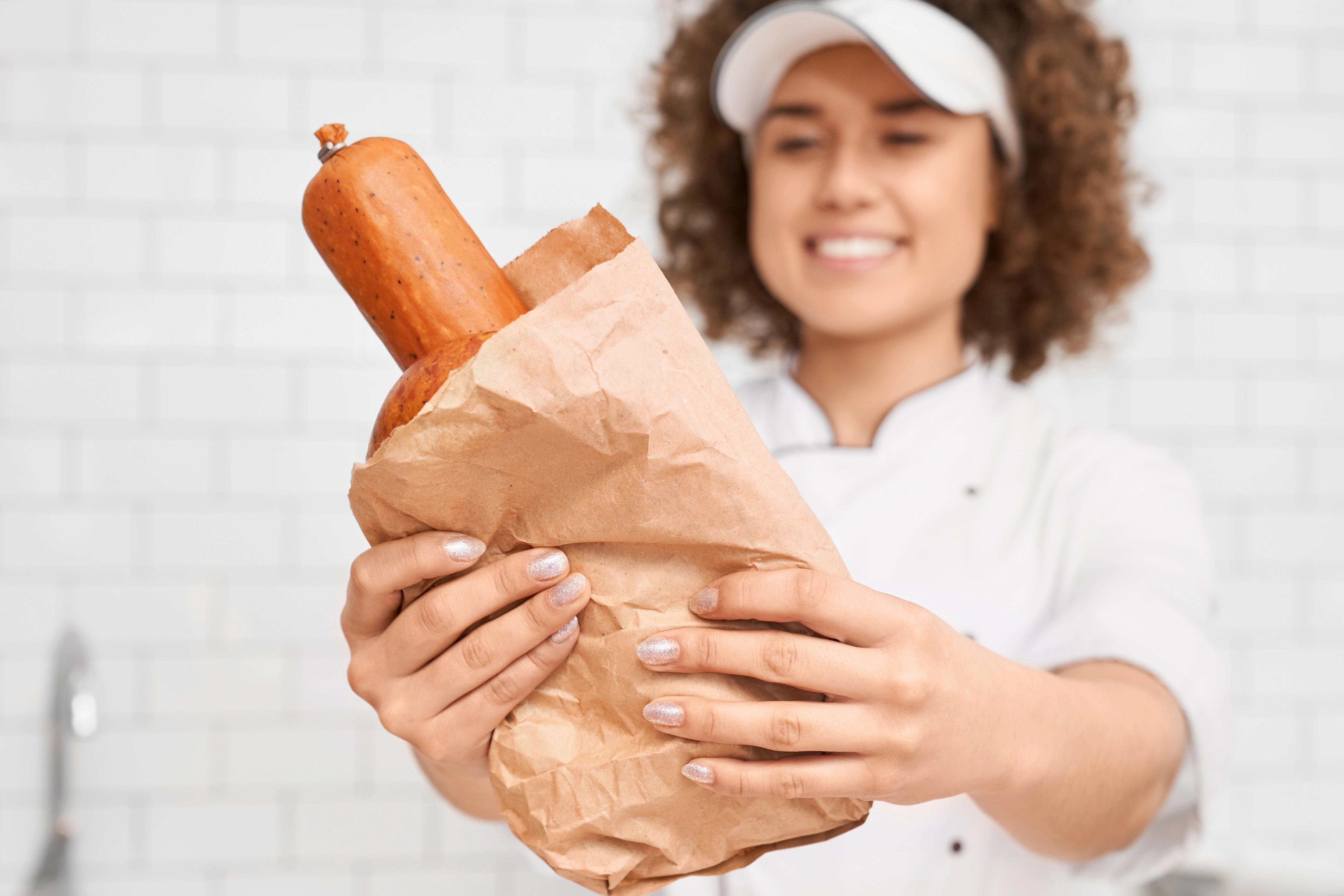 Metzgerin, die Wurst in einem Metzgerfaltenbeutel präsentiert.