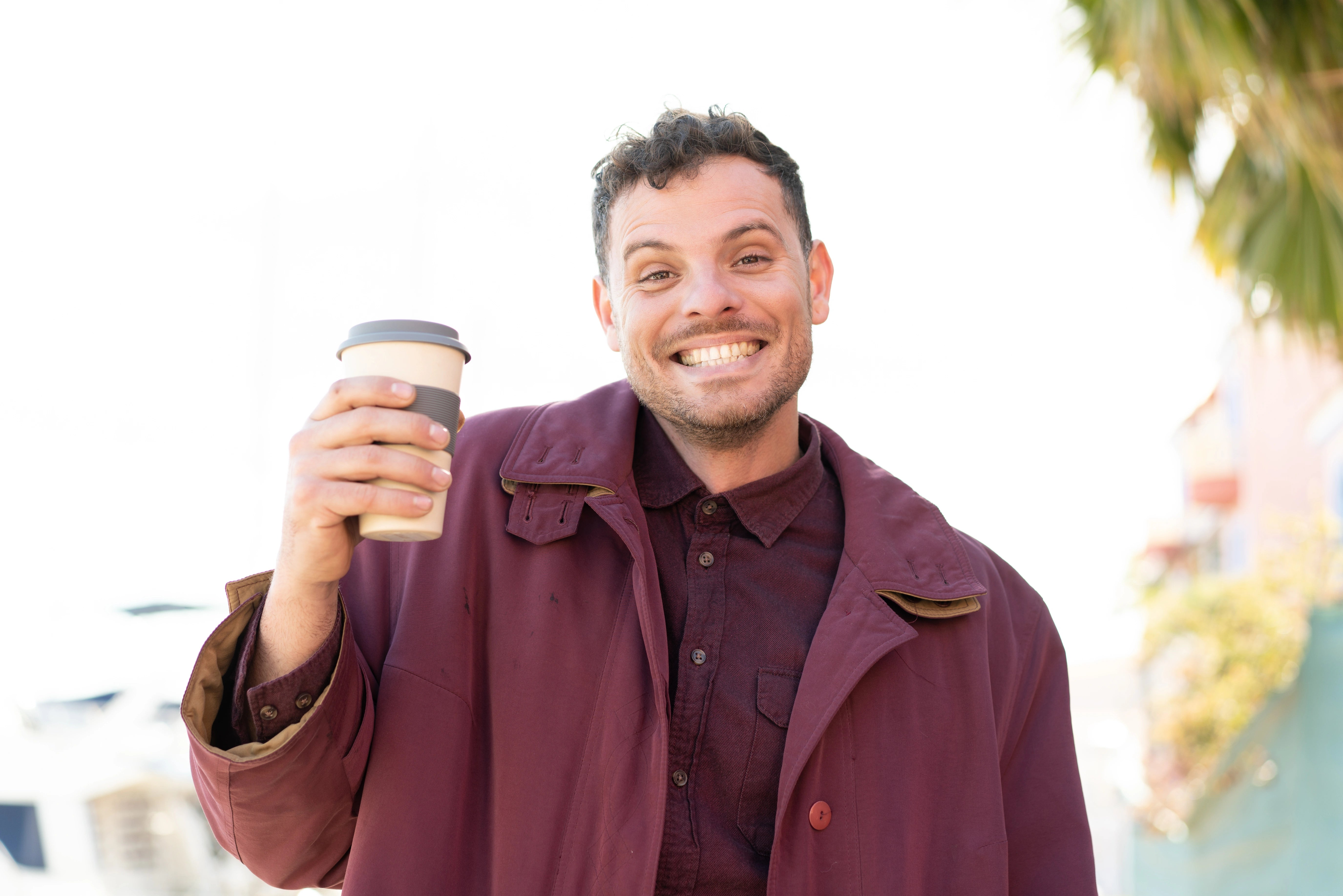 Junger Mann, der einen Kaffeebecher in der Hand hält und lächelt.