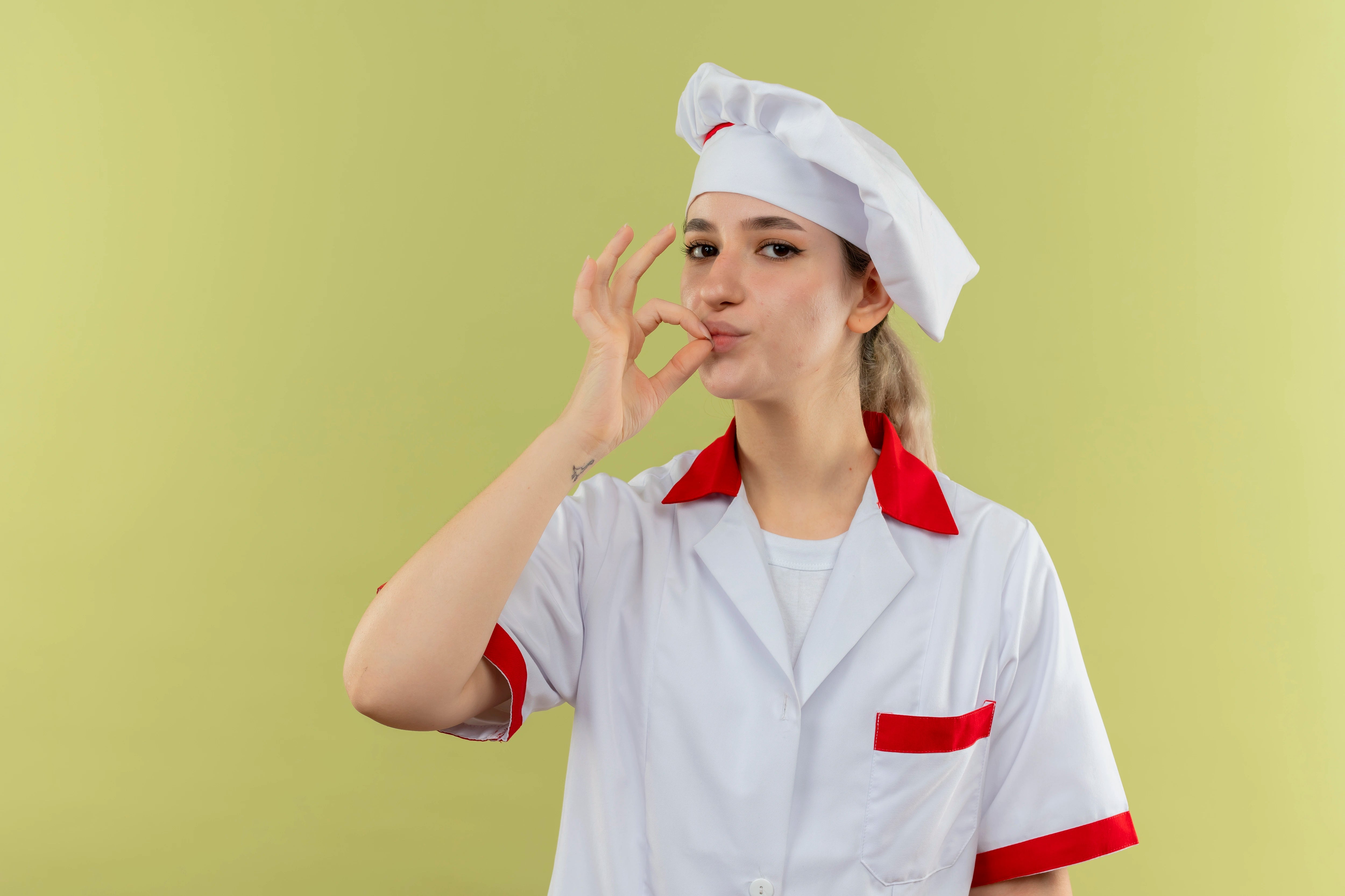 Frau in Gastronomie-Berufsbekleidung vor neutralem Hintergrund.