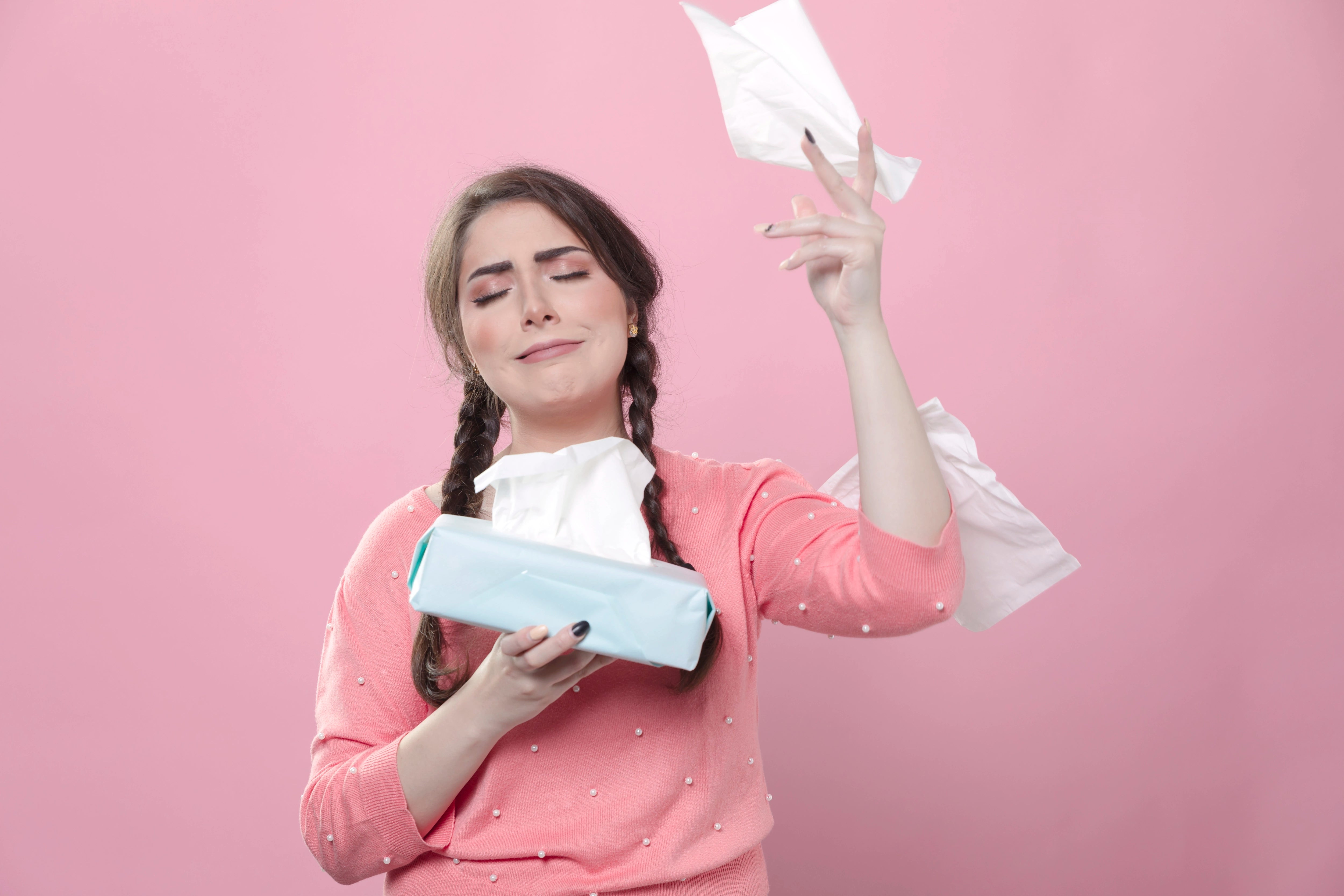 Junge Frau mit einer Taschentuch Box in der Hand auf rosa Hintergrund.