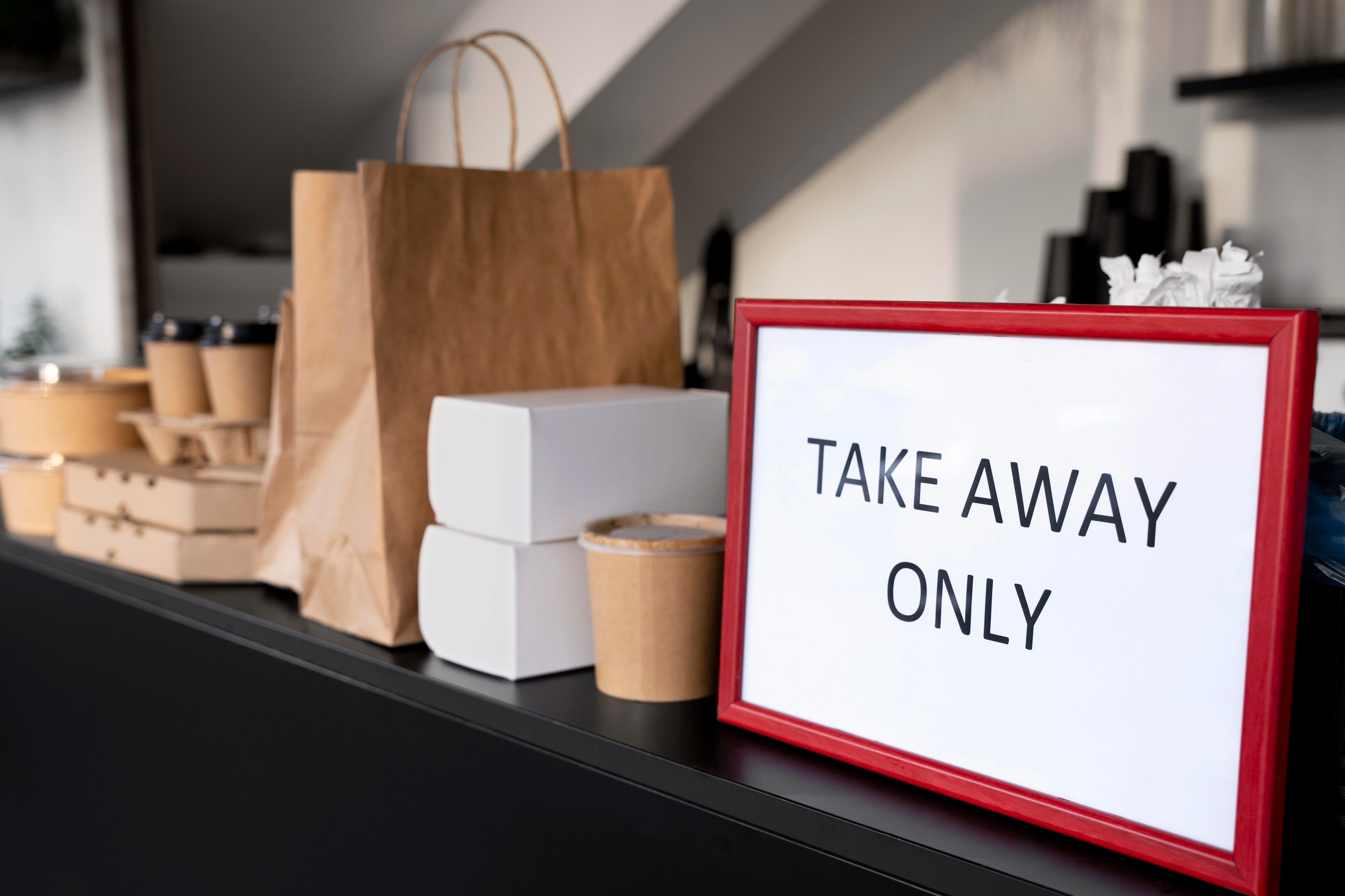 Ein Schild, auf dem "Take Away Only" steht, und Take Away Verpackungen auf einem Tresen.