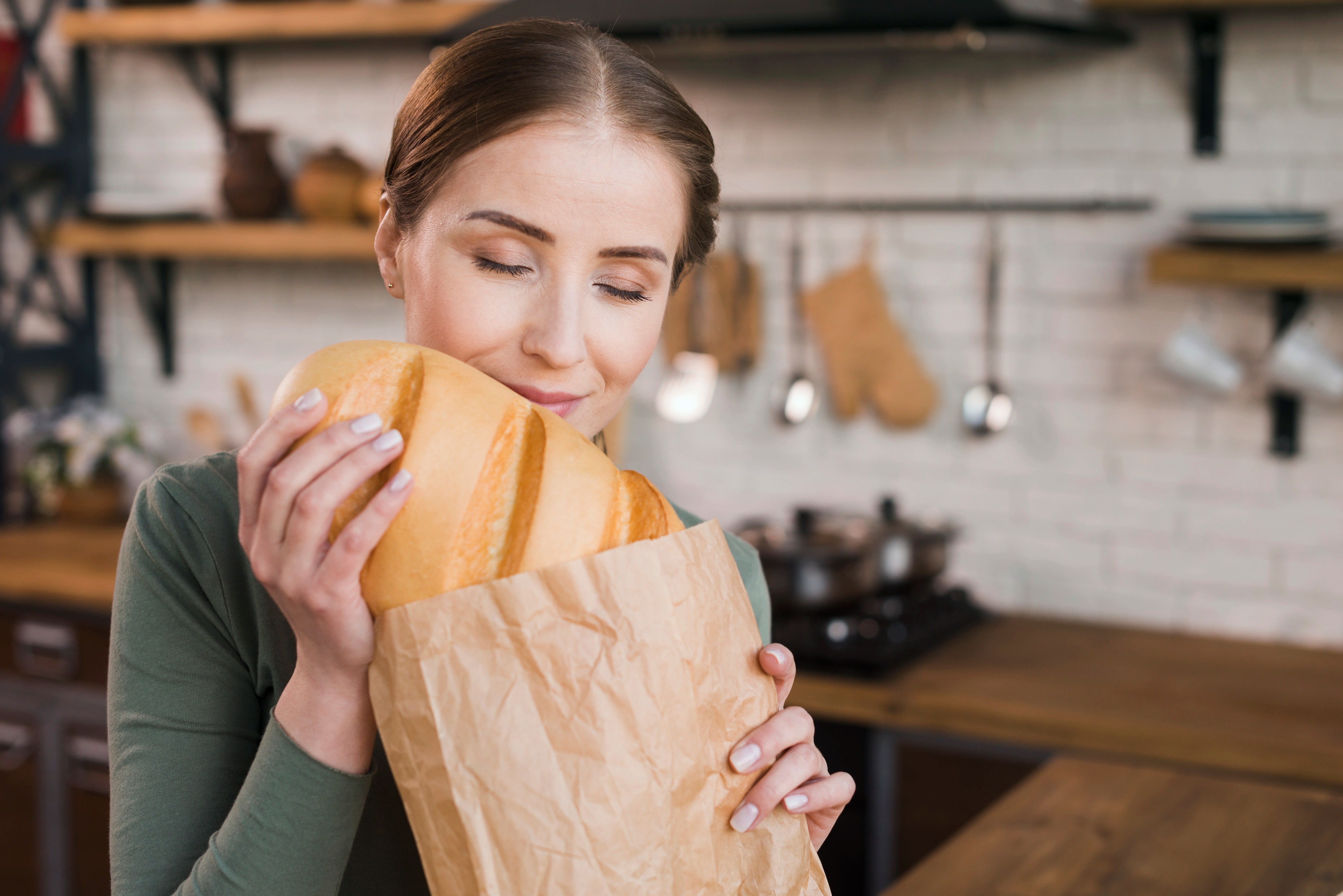 Frau riecht an einem großen Weißbrot aus einer Brotpapiertüte.