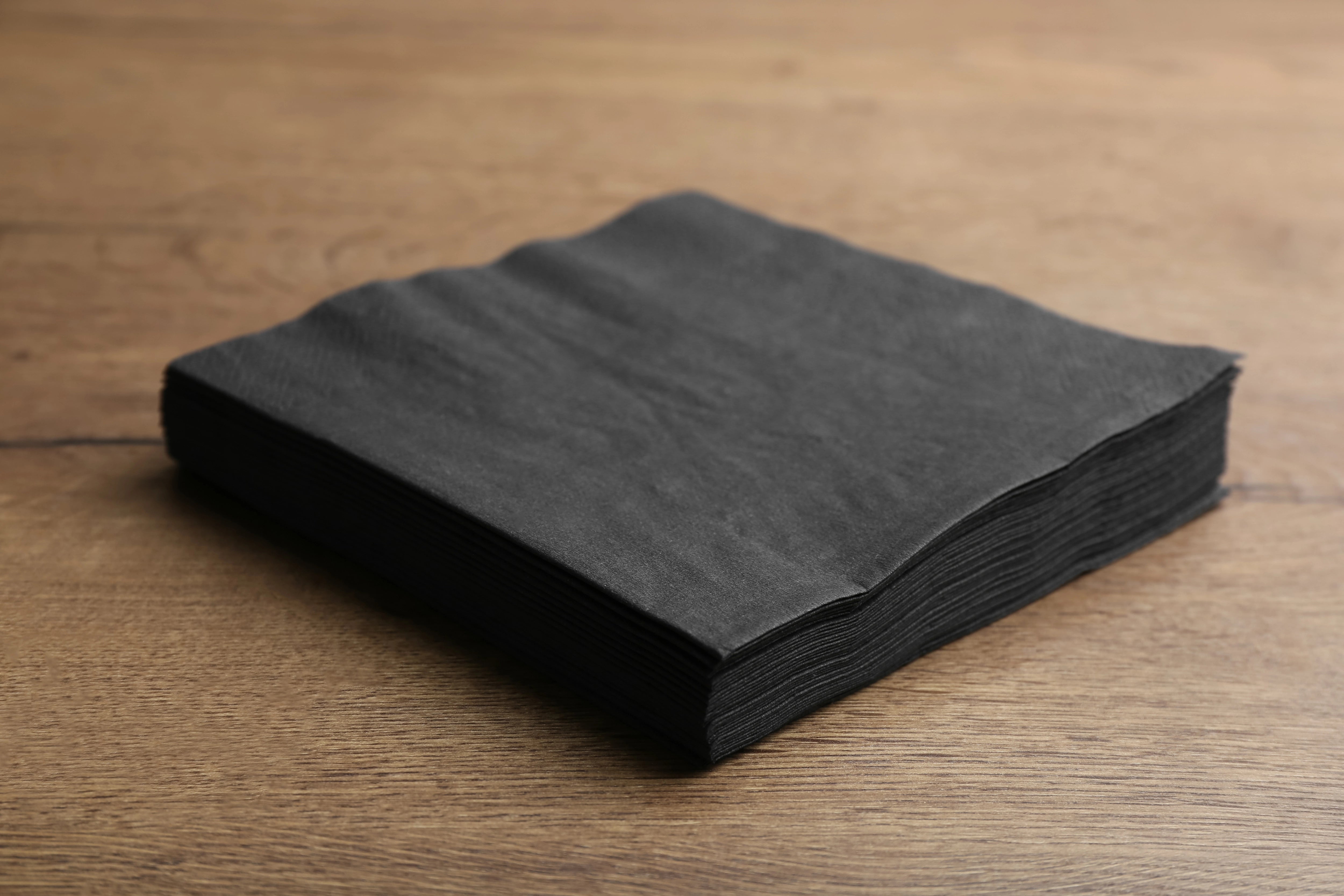 Schwarze Airlaid Servietten 40x40 auf einem Holztisch.