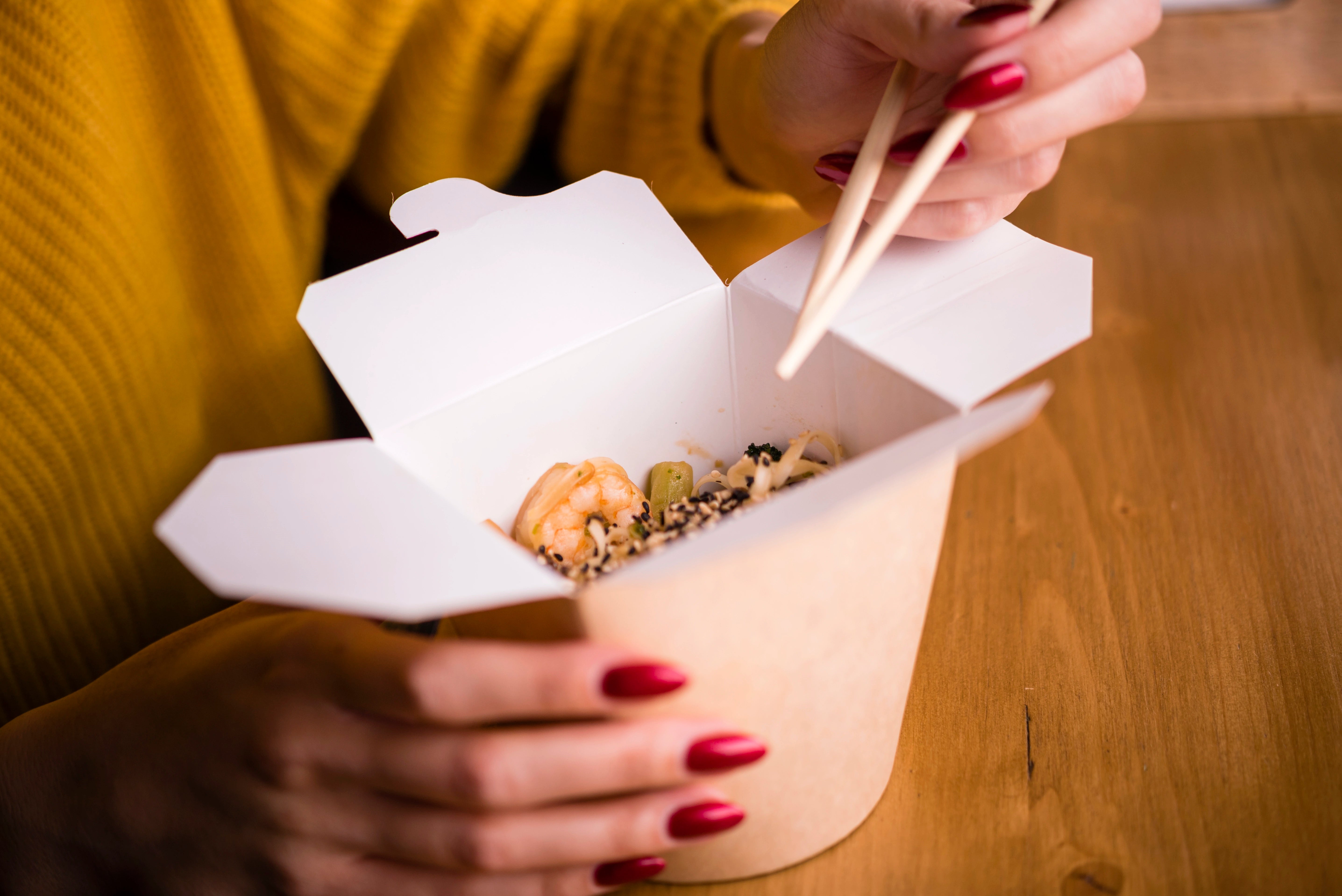 Frau sitzt mit einer Asia Box am Esstisch.